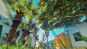 A building with a yellow facade and a blue door, surrounded by palm trees and greenery. - Porticello Sea Village • Three-room apartment (Puglia)