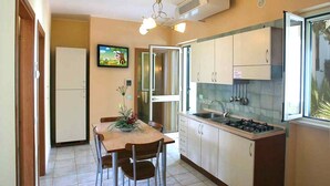 A compact kitchen with a dining table, chairs, a stove, and cabinets. - Porticello Sea Village • Three-room apartment (Puglia)