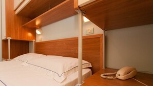 A hotel room with a wooden headboard, a bed with white linens, a bedside telephone, and a wall-mounted light fixture. - Porticello Sea Village • Three-room apartment (Puglia)