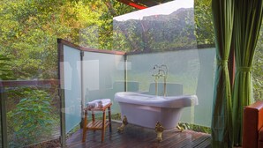 A glass-enclosed outdoor bathroom with a bathtub, a wooden stool, and a towel. - The Arboreal Resort (Mawal)