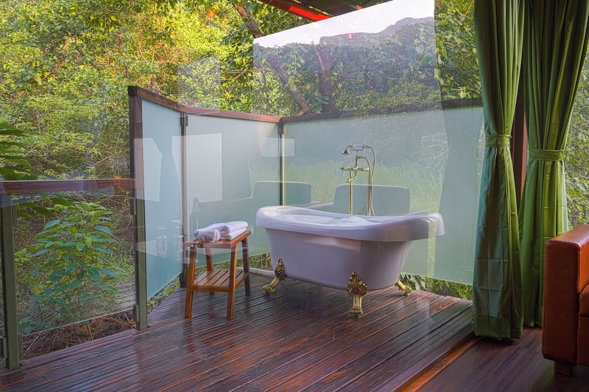 Ein vom Wind geschütztes Badezimmer im Freien mit einer Badewanne, einem hölzernen Hocker und einem Handtuch.