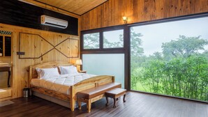 A wooden bedroom with a large bed, a bench, and a view of greenery outside. - The Arboreal Resort (Mawal)