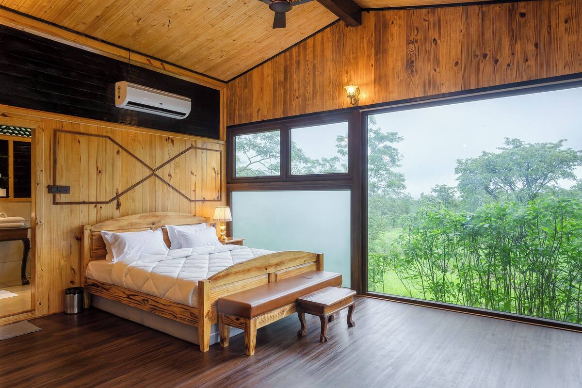 Ein Schlafzimmer aus Holz mit einem großen Bett, einer Bank und Blick ins Grüne.