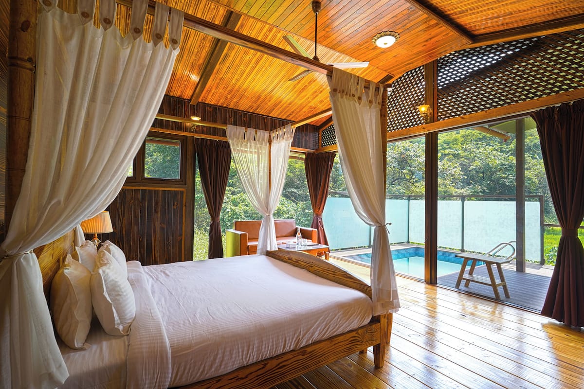 Ein Zimmer mit Holzboden, einem Bett, einem Sessel und Blick auf einen Pool.