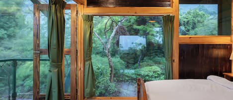 A wooden cabin room with a bed, large windows, and a view of a forest.