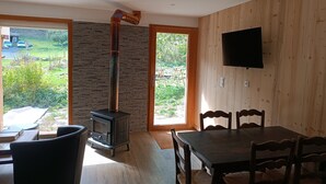Un interior moderno con estufa de leña, comedor con sillas y televisor montado en la pared.