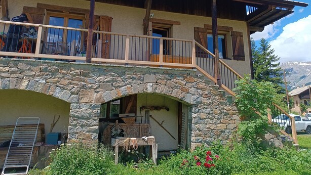 Una casa de piedra con balcón, vigas de madera y un arco de piedra.