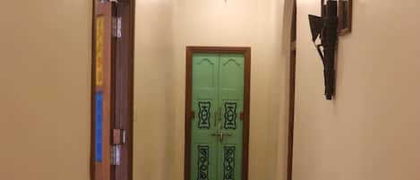 A hallway with a green door, a trash bin, and a light fixture.