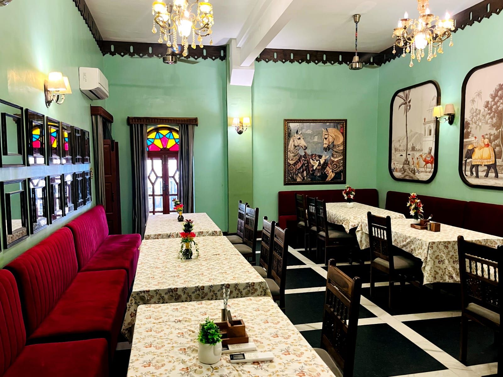 Un restaurante con una barra larga, asientos rojos, candelabros y decoración en las paredes.