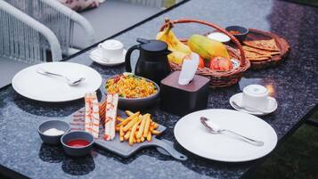 Una mesa servida con varios platos, incluyendo arroz, papas fritas y un sándwich a la parrilla, junto con una cafetera y una cesta de frutas.
