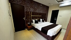 A modern hotel room with a large bed, a wooden nightstand, a dark headboard, and a patterned wall. - Hotel Apple INN (Indore)