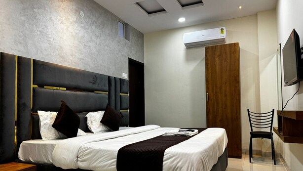 A modern bedroom with a large bed, a wooden wardrobe, a desk, and a television. - Hotel Apple INN (Indore)