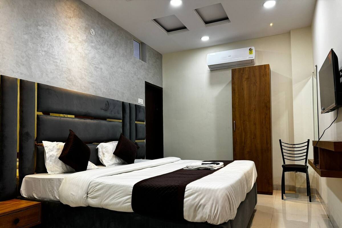 A modern bedroom with a large bed, a wooden wardrobe, a desk, and a television.