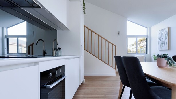 A modern kitchen with white cabinetry, a black stove, and a wooden staircase. - Cosy Riverside Escape with River Views (Riverside)