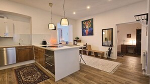 A modern kitchen with wooden cabinets, a central island, pendant lights, and a dining area with a table and chairs. - Red Palm - 100m2 - cozy, central, stylish (Wien)