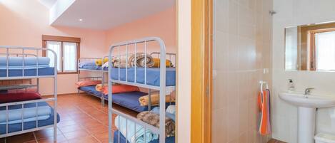 A dormitory room with bunk beds, a bathroom with a sink, and a window.