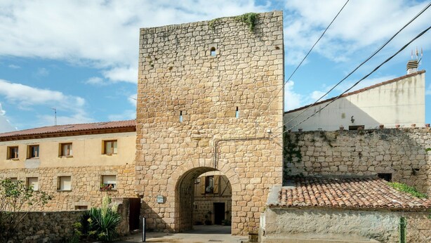 Une tour de pierre dotée d’une entrée en arc de cercle, entourée d’immeubles aux toits couverts de tuiles.