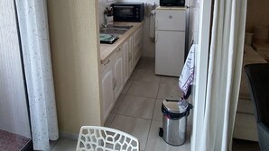 A compact kitchen with a microwave, oven, and refrigerator. A small trash bin is visible near the entrance.