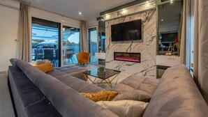 Ein modernes Wohnzimmer mit einer großen, grauen Couch, einem Glastisch und einem an einer Marmorwand montierten Flachbildfernseher.