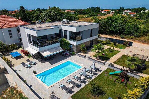 Ein modernes, zweistöckiges Haus mit Schwimmbad, Außenbereich und Spielplatz.