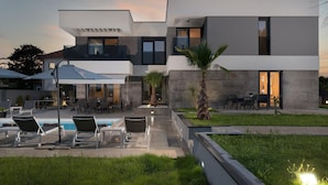 Ein modernes, zweistöckiges Haus mit Pool, Sitzgelegenheit im Freien und einem gepflegten Garten.