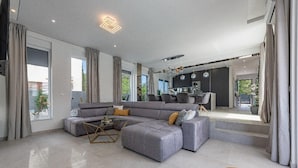 Ein modernes Wohnzimmer mit einem grauen Ecksofa, einem Couchtisch und einem Essbereich im Hintergrund.
