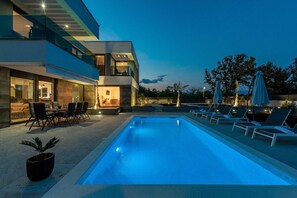 Ein moderner Poolbereich mit rechteckigem Pool, Liegestühlen und einer Essgegend mit Tisch und Stühlen.