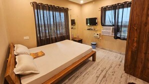 A bedroom with a bed, curtains, a television, a mirror, and a window. - HOTEL AVAAS TripandTrip (Puri)