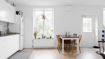 Ett modernt kök med vita skåp, ett matbord med trästolar och ett fönster med utsikt över ett hus.