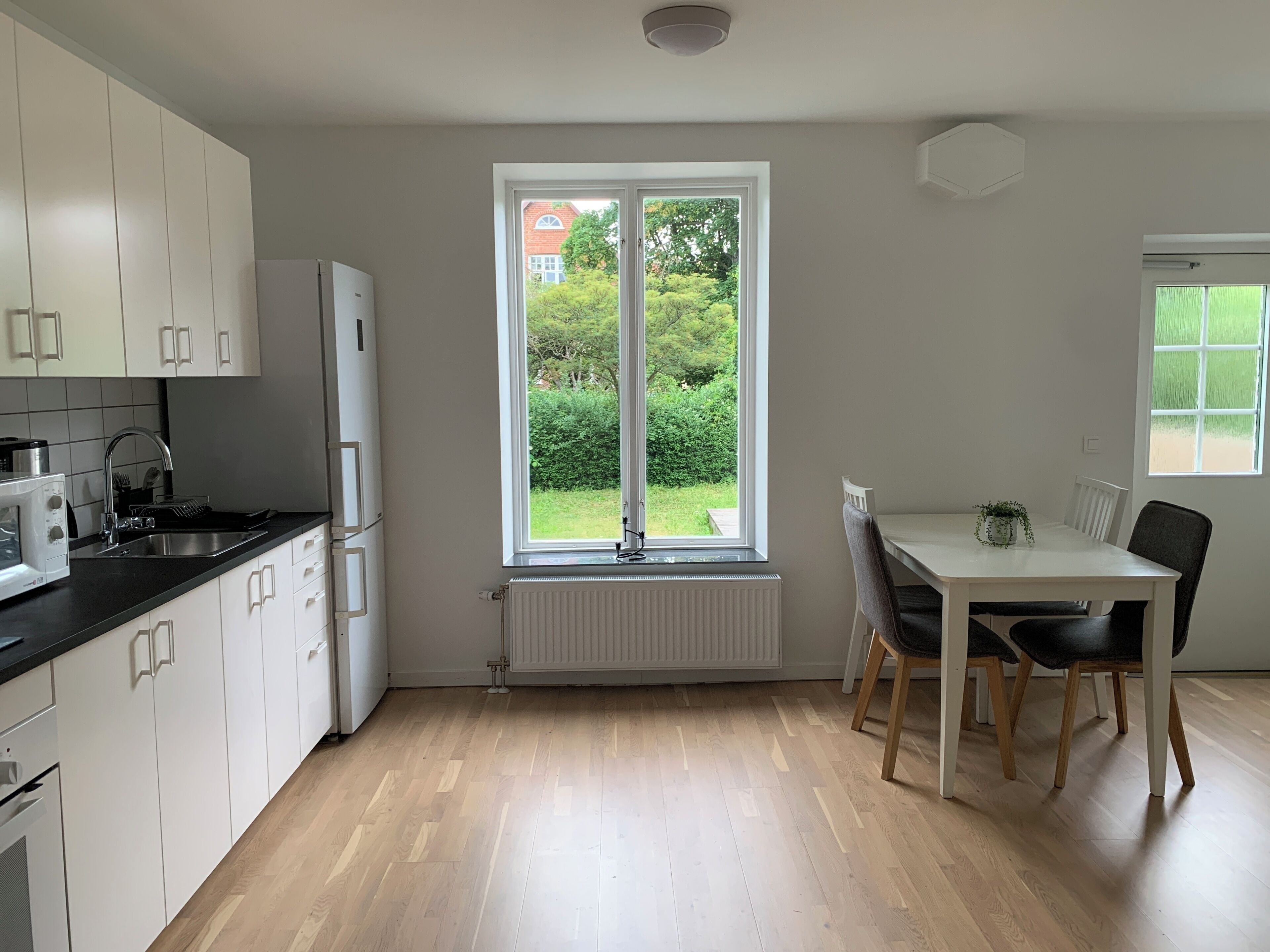 A modern kitchen with white cabinets, a built-in oven, and a window overlooking a garden.