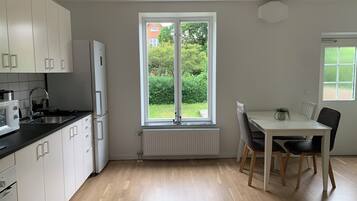 A modern kitchen with white cabinets, a built-in oven, and a window overlooking a garden.