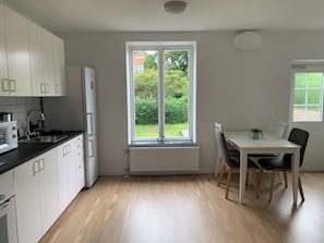 A modern kitchen with white cabinets, a built-in oven, and a window overlooking a garden. - Villa Nova (Lund)