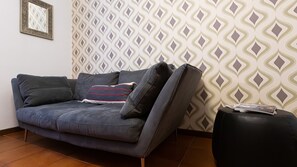Una sala de estar moderna con un sofá gris, un cojín a rayas y un otoman negro.