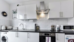 Una cocina moderna con armarios blancos, extractor de acero inoxidable, horno empotrado, lavadora y microondas.