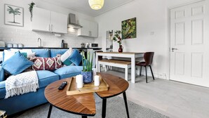 Una sala de estar moderna con un sofá azul, una mesa de centro de madera y un comedor con una mesa y sillas blancas.