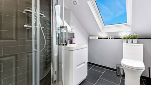 Un baño moderno con cabina de ducha de vidrio, inodoro blanco y una pequeña ventana sobre el inodoro.