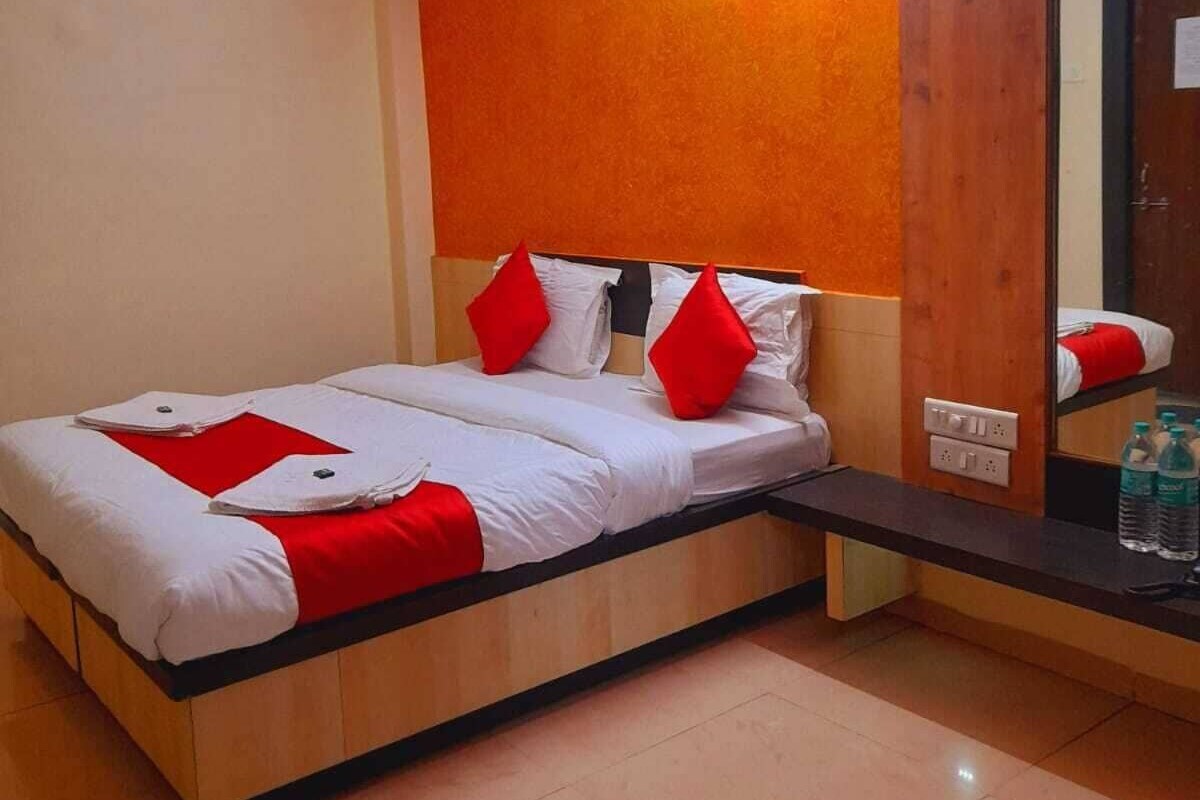 A hotel room with a bed, a ceiling fan, a mirror, and a nightstand with water bottles.