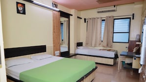 A room with two beds, a mirror, a window with curtains, a desk, and an air conditioning unit. - Hotel Saikrupa (Rahata)
