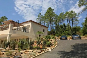 A two-story house with a balcony, surrounded by a landscaped garden with various plants and a stone wall.