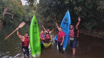 A group of people standing in a river with kayaks, wearing life jackets.