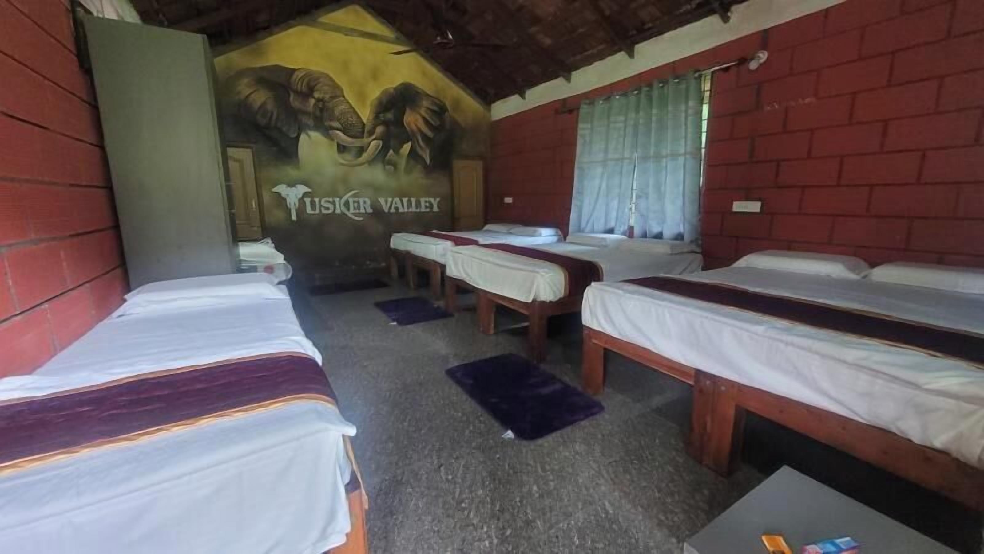 A room with three single beds, a mural of an elephant, and a sign reading "Tusker Valley".