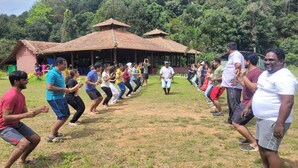 A group of people participating in an outdoor activity in a grassy area with a pavilion in the background. - Tusker Valley Resort (Sakleshpur)