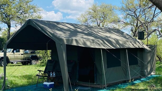 A tent with a canvas roof, set up on a grassy area with a blue tarp underneath. - Moremi Enclave Resort  (Maun)