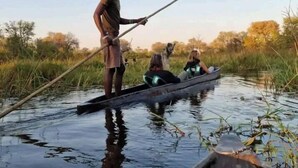 A person standing in a boat on a calm body of water, holding a long pole. - Moremi Enclave Resort  (Maun)