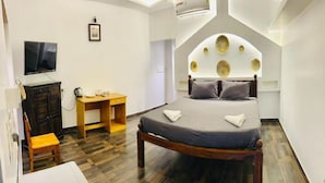 A bedroom with a bed, a desk, a chair, and a TV. - The French Villa Elite (Puducherry)