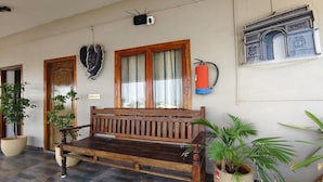 A wooden bench with a fire extinguisher mounted on the wall, potted plants, and a door with a decorative glass panel. - The French Villa Elite (Puducherry)
