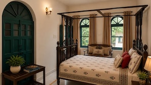 A four-poster bed with a floral bedspread, a nightstand with a lamp, a potted plant, and a green door. - AM Hotel Kollection Maangarh Ratlam (Ratlam)