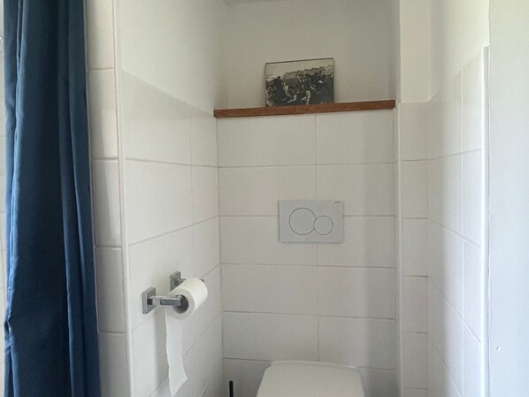 A small, tiled bathroom with a toilet, a towel holder, and a picture frame on the wall.