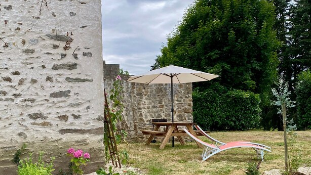 A stone wall, a wooden table with a bench, and a picnic table with an umbrella in a garden setting.