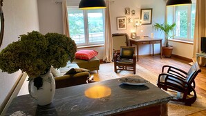 A living room with a sofa, a dining table with a vase of flowers, a chair, and a television.
